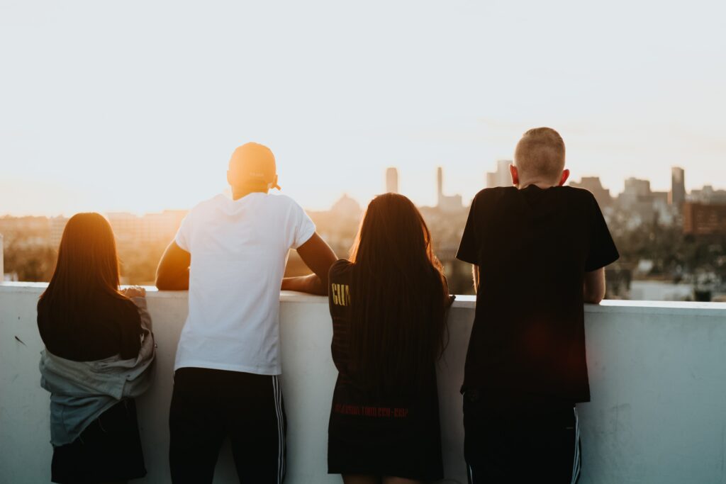 Vier Personen stehen im Sonnenuntergang auf einem Balkon. Im Hintergrund ist eine Stadt erkennbar.